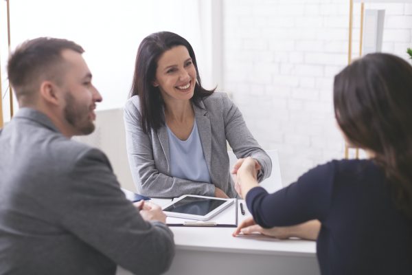 Positive insurance broker handshaking with young couple